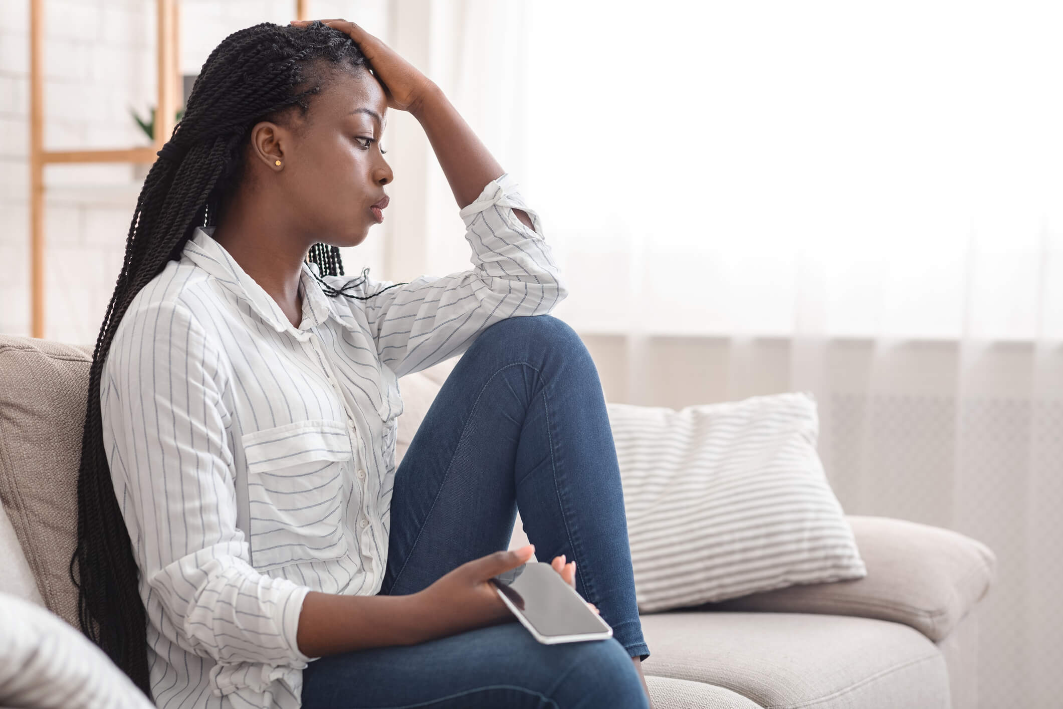 upset woman sitting on couch with cellphone